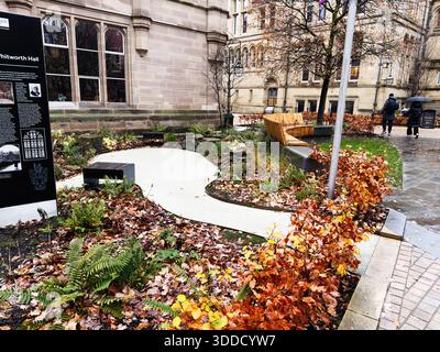 Manchester, Regno Unito - 06 dicembre 2025: Giardino autunnale nel campus di Manchester con posti a sedere, cartello e persone che passeggiano. Foto Stock