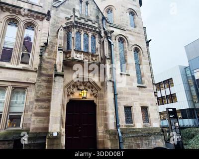 Manchester, Regno Unito - 06 dicembre 2025: Edificio storico di Manchester con finestre ad arco, porta scolpita e una calda lanterna. Foto Stock