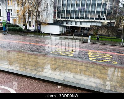 Manchester, Regno Unito - 06 dicembre 2025: Una strada bagnata di Manchester con uffici moderni, pavimentazione e segnaletica stradale gialla. Foto Stock