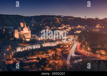 Il centro storico di Tbilisi brilla di notte con sentieri leggeri provenienti da automobili in movimento, che mostrano la chiesa di Metekhi Foto Stock