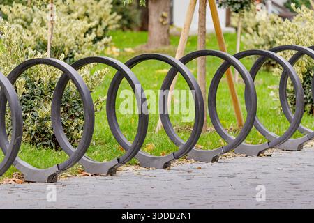Moderno portabiciclette con elementi metallici circolari che forniscono soluzioni di parcheggio su un sentiero asfaltato in un parco cittadino Foto Stock