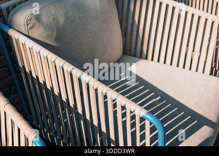 Moderna poltrona da patio con cinghie intrecciate e morbidi cuscini, crogiolandosi nella calda luce del sole e proiettando ombre forti e invitanti Foto Stock