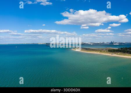 Prospettiva elevata del Pont de l'Ile de Re che si estende attraverso le vivide acque turchesi verso la terraferma, con litorale sabbioso e nuvole di cumulus sparse in alto. La scena mette in evidenza il paesaggio costiero aperto e l'atmosfera tranquilla della Charente-Maritime nella Francia occidentale. Foto Stock