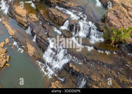 La prospettiva aerea mostra il flusso d'acqua su rocce vulcaniche stratificate e piccole sporgenze a Tad lo nel sud del Laos. La scena mette in risalto le texture contrastanti di pietra e le dolci cascate sotto la luce del giorno. Foto Stock