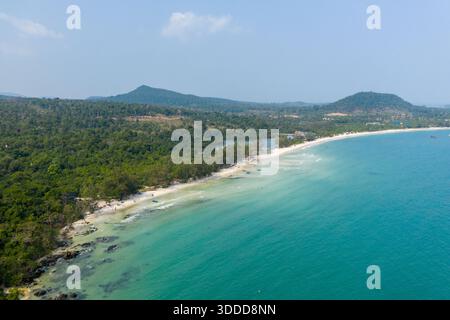 L'ampia vista aerea mostra il delicato arco di Long Set Beach delimitato da acque turchesi cristalline e da una lussureggiante foresta verde sull'isola di Koh Rong, Cambogia. Colline ondulate e barche sparse completano questa tranquilla costa tropicale. Foto Stock