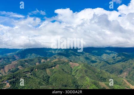 Colline verdi ondulate e creste boscose si estendono sotto una vasta distesa di spesse nuvole bianche e un vivace cielo blu nella campagna tra Vang Vieng e Phou Khoun, Laos. Il paesaggio presenta tortuose strade di montagna, pendii strutturati e un gioco dinamico di luci e ombre sul terreno. Foto Stock