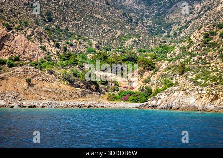 Montagne paesaggi suggestivi e case in pietra sul mare dell'isola di Ikaria in estate in Grecia con vista sulla natura dei fiori di oleandro vicino a Karkinagri Foto Stock
