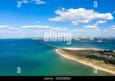 Ampia vista aerea del Pont de l'Ile de Re che si estende attraverso le vivide acque turchesi verso la terraferma, con coste sabbiose e nuvole di cumulus sparse in alto. L'immagine mette in risalto il mare aperto e la tranquilla atmosfera costiera di Charente-Maritime nella Francia occidentale. Foto Stock