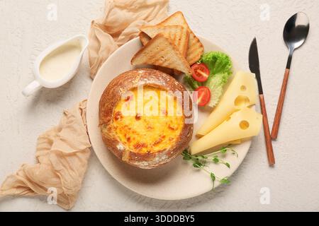Zuppa di formaggio nel recipiente del pane con lattuga, toast, verde e pomodoro su sfondo chiaro Foto Stock