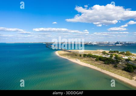 Ampia vista aerea del Pont de l'Ile de Re, che si estende attraverso l'acqua blu vivace verso la terraferma, con litorale sabbioso, vegetazione costiera e nuvole di cumulus sparse in alto. La composizione mette in risalto il mare aperto e l'atmosfera tranquilla della Charente-Maritime nella Francia occidentale. Foto Stock