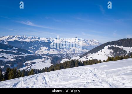 Ampia vista invernale sulle colline innevate, sulle foreste di pini e sulla valle di Megeve, con spettacolari cime montuose che si innalzano sotto un cielo azzurro. La luce del sole riproduce la neve incontaminata e crea un'atmosfera alpina luminosa e rinvigorente. Foto Stock