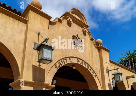 Una vivace facciata in stucco giallo a Santa Barbara con un arco, data storica, lanterne decorative e un albero di palma sotto il cielo blu. Foto Stock