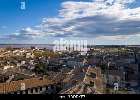 Ampia vista sui tetti di terracotta di Aigues-Mortes con bastioni in pietra medievali e paludi di sale rosa sotto un cielo spettacolare pieno di nuvole sparse. Foto Stock