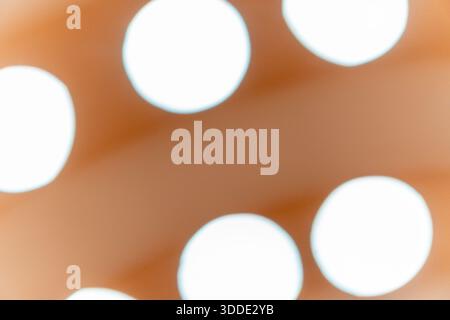 Uno sfondo astratto morbido e sfocato caratterizzato da macchie bokeh circolari bianche luminose su una calda superficie arancione e marrone. Foto Stock