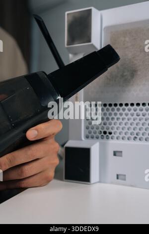 Colpo ritagliato verticale del riparatore che aspira la polvere dal filtro di scarico del pc desktop e dal pannello a rete durante la manutenzione ordinaria dell'unità di sistema per evitare che ciò accada Foto Stock