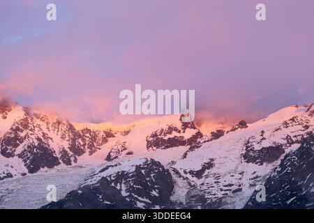 Il caldo rosa e arancione alpenglow illumina le cime innevate e le aspre creste del Monte bianco del Tacul, con morbide nuvole che attraversano il suggestivo paesaggio alpino. Foto Stock