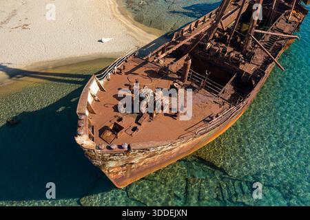 Vista aerea dettagliata della prua arrugginita del relitto di Dimitrios che riposa in un mare turchese poco profondo e trasparente accanto a una costa sabbiosa vicino a Gythio, in Grecia. La luce del sole rivela texture corrose e il contrasto tra metallo e acqua incontaminata. Foto Stock