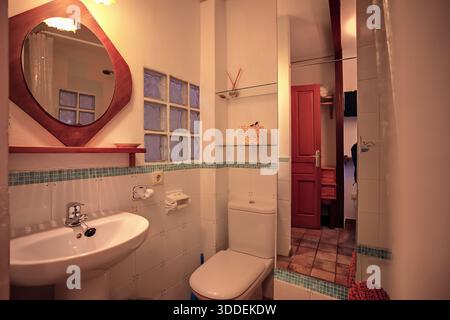 Bagno accogliente con lavandino, WC e porta rossa in un ambiente caldo e intimo Foto Stock