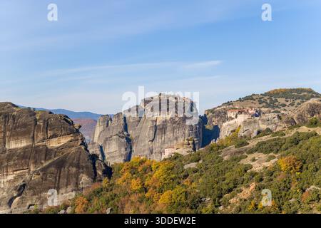 Vista elevata dei monasteri di Varlaam e Grand Meteore arroccati su torreggianti rocce di arenaria a Meteora, in Grecia, incorniciati da un vivace fogliame autunnale e da un cielo limpido. Foto Stock