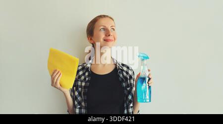 Concetto di pulizia della casa - casalinga o pulitrice, giovane donna sorridente che tiene a casa un panno in microfibra asciutto e una bottiglia spray detergente || modello rilasciato Foto Stock