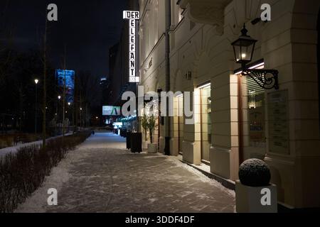 Ambientazione notturna invernale nel centro di Varsavia con la facciata illuminata dell'edificio storico e il marciapiede coperto di neve. Foto Stock