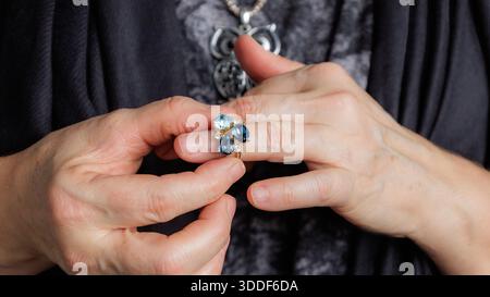 Primo piano delle mani che mostra un anello blu in pietra preziosa contro un tessuto scuro. Foto Stock