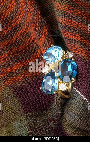 Primo piano di un anello blu in pietra preziosa appoggiato su tessuto testurizzato. Foto Stock