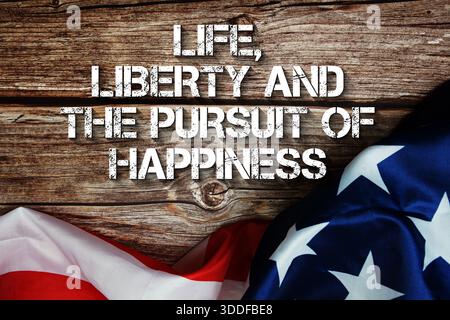 Messaggio di testo Life, Liberty and the Pursuit of Happiness con bandiera USA su sfondo in legno Foto Stock
