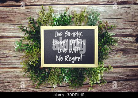 "Vivere semplicemente, ridere spesso, amare senza rimpianti" citazione ispirativa sulla lavagna circondata dal verde e dallo sfondo in legno rustico Foto Stock