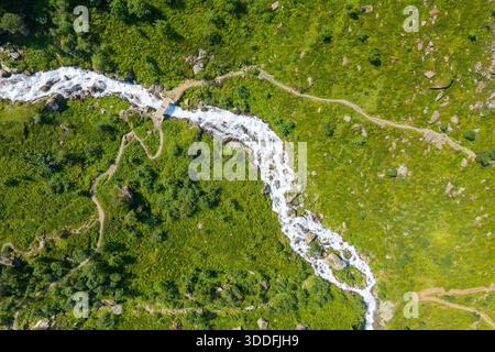 Vista aerea di una stretta passerella in legno che attraversa un ruscello che scorre velocemente tra lussureggianti colline verdi e sentieri escursionistici tortuosi nella campagna dei Pirenei in una soleggiata giornata estiva. Foto Stock