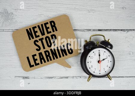 Non smettere mai di imparare il testo con la sveglia su sfondo di legno Foto Stock