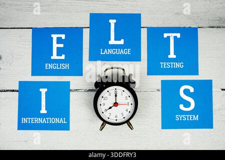 IELTS International English Language Testing System con sveglia su fondo in legno Foto Stock