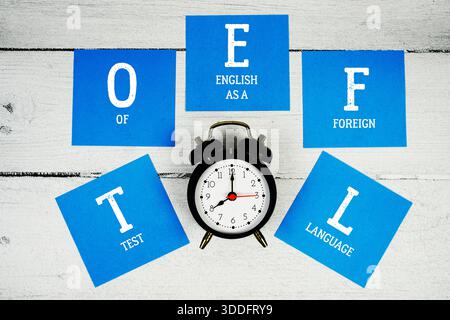 TOEFL test of English as a Foreign Language con sveglia su sfondo in legno Foto Stock