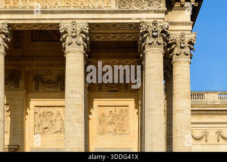 Primo piano di capitelli corinzi ornati e intricati fregi di pietra sulla facciata del Pantheon a Parigi, illuminati dalla luce del sole e adagiati su un cielo azzurro. Foto Stock