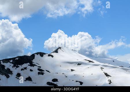 L'Aiguillette des Houches mostra una vetta dolcemente in pendenza con macchie di neve che scioglie e rocce scure esposte sotto un cielo luminoso pieno di morbide nuvole di cumulus. Foto Stock