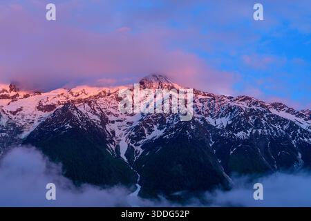 l'alpenglow rosa e viola illumina la vetta innevata del Monte bianco, con spettacolari nuvole e pendii boscosi scuri sottostanti nella tranquilla atmosfera serale. Foto Stock