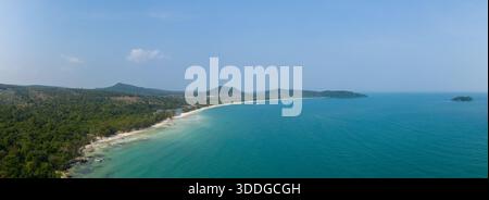 L'ampia vista panoramica mostra l'ampia curva di Long Set Beach sull'isola di Koh Rong, in Cambogia, dove la sabbia bianca incontra il mare turchese. Lussureggiante foresta e dolci colline confinano con la tranquilla costa sotto un cielo blu cristallino. Foto Stock