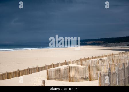 Lagoa de Albufeira Sesimbra Portogallo dicembre 25 2025. Recinzioni di sabbia in legno costeggiano le dune costiere sopra un'ampia spiaggia sabbiosa sotto un cielo scuro. Foto Stock