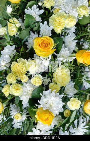 Fresco allestimento floreale caratterizzato da vivaci rose gialle circondate da crisantemi bianchi e garofani gialli tenui, completato da un lussureggiante fogliame Foto Stock
