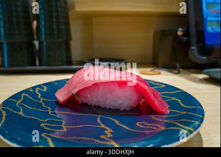 Un singolo pezzo di nigiri di tonno fresco e' posto elegantemente su un piatto blu lucido caratterizzato da motivi della linea d'oro, posto su un bancone di legno chiaro in un moderno ristorante di sushi ad Osaka. Foto Stock