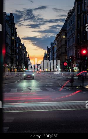 Lunga esposizione al traffico su un viale della città al tramonto, con sentieri leggeri, lampioni ed edifici storici sotto un cielo colorato al tramonto. Foto Stock