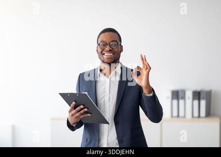 Ritratto di allegro psicologo maschio nero che mostra un buon gesto, raccomandando aiuto professionale in clinica Foto Stock