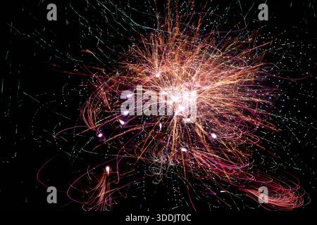 Fotografia astratta a lunga esposizione di fuochi d'artificio che creano sentieri luminosi densi e colorati con raffiche luminose contro un cielo notturno nero profondo. Dynami Foto Stock