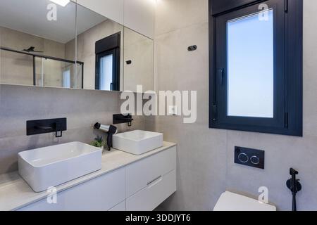 Bagno moderno e minimalista con doppio lavabo, eleganti rubinetti neri e grandi armadi a specchio Foto Stock