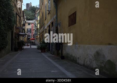 Vicolo stretto con un muro ricoperto di edera e una scogliera in lontananza con un castello sulla sua sommità, incorniciato dagli edifici sulla strada stessa, in una Foto Stock