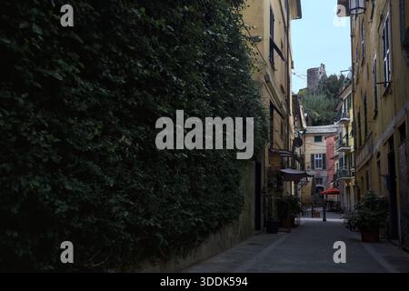 Vicolo stretto con un muro ricoperto di edera e una scogliera in lontananza con un castello sulla sua sommità, incorniciato dagli edifici sulla strada stessa, in una Foto Stock