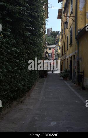 Vicolo stretto con un muro ricoperto di edera e una scogliera in lontananza con un castello sulla sua sommità, incorniciato dagli edifici sulla strada stessa, in una Foto Stock