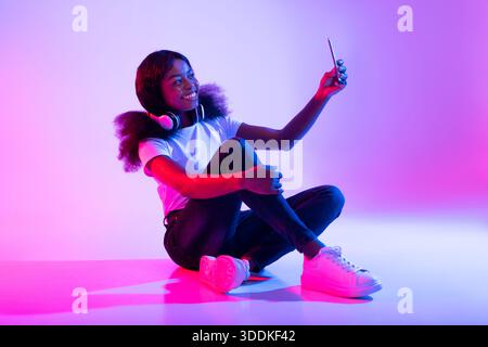 Giovane donna nera che si diverte con le luci al neon mentre si prende un selfie per i suoi social media Foto Stock