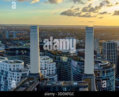 Vista aerea di due dei famosi camini bianchi della centrale elettrica di Battersea, circondati da moderni edifici residenziali ricurvi al tramonto Foto Stock