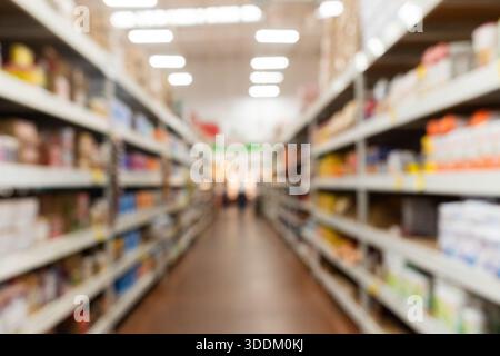 Corridoio lungo e sfocato in un supermercato con scaffali pieni di generi alimentari e altri prodotti. Sfondo. Foto Stock